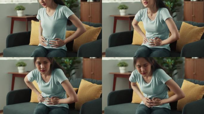 一位年轻的亚洲女性，正因胃痛而坐在家里客厅的沙发上。