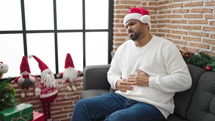 一个非洲裔美国人在家里戴着圣诞帽忍受着胃痛