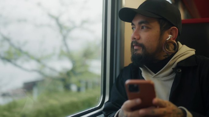 一名放松的亚洲男子在瑞士的火车上用手机阅读和聊天信息。