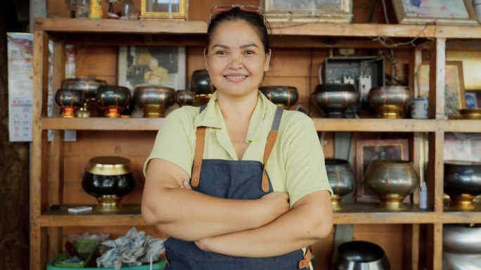 曼谷，一位手工艺品店主抱臂微笑，为自己的小生意感到自豪。