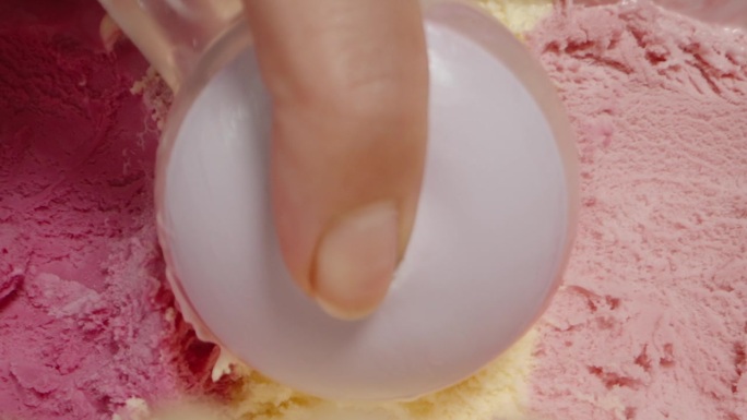 微距特写，用特制的冰淇淋勺从容器中舀出五彩缤纷的粉色冰淇淋。