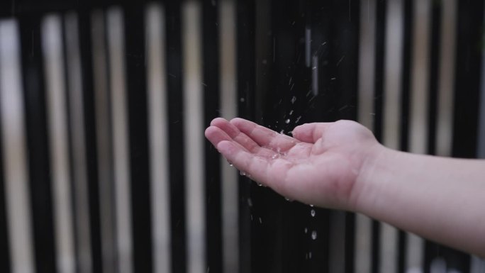 一个男人在大雨中伸出手，手掌张开，直到他的手里有一个小水坑，他站在房子的前院。雨天从人手上滴下的雨水