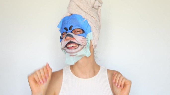 面部护理和美容护理。小女孩在洗澡后用毛巾敷在头上，用动物嘴型面膜在白色背景上进行保湿。