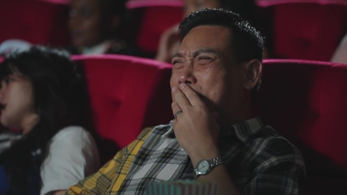 亚洲男人在电影院看浪漫爱情电影时哭了。亚洲男人坐在电影院的座位上看悲伤的电影，哭了。感觉,哭