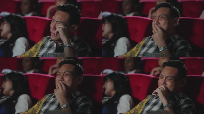 亚洲男人在电影院看浪漫爱情电影时哭了。亚洲男人坐在电影院的座位上看悲伤的电影，哭了。感觉,哭