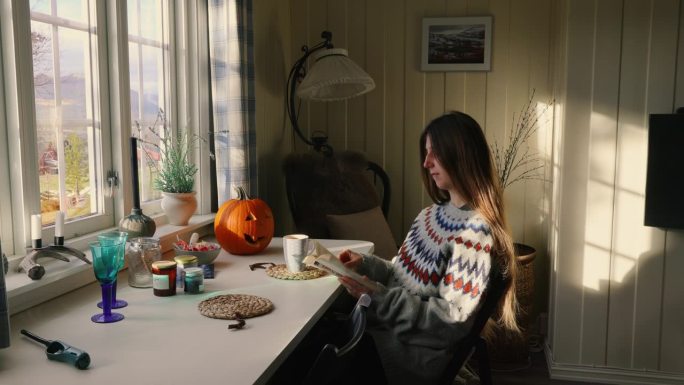 穿着羊毛衫的女人在家里读着书，喝着咖啡，想着万圣节的早晨