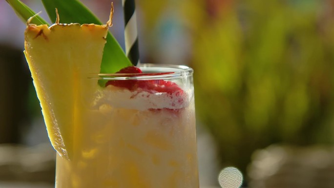 将菠萝片放入冰镇椰林酒杯中，以热带秸秆为背景