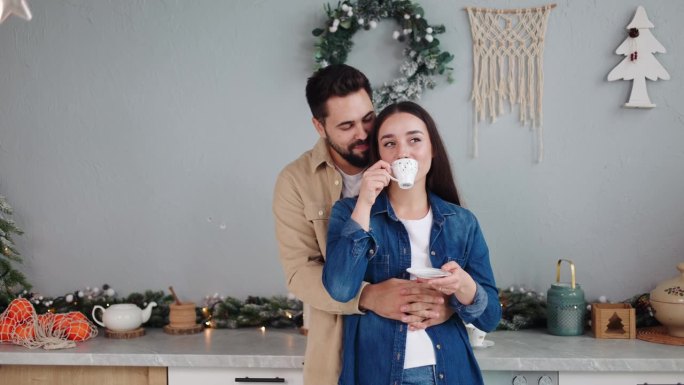 在圣诞灯火辉煌的厨房里，一位慈爱的男人热情地拥抱着端着咖啡的妻子。在节日的气氛中，他们一起分享新年的