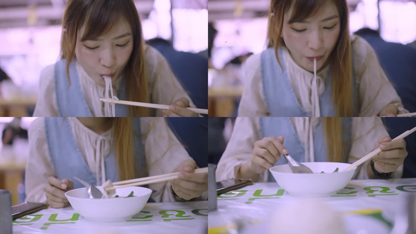 一位饥饿的亚洲妇女坐在露天面馆里，用筷子和勺子享用着一碗热腾腾的米粉汤，背景是很多人。