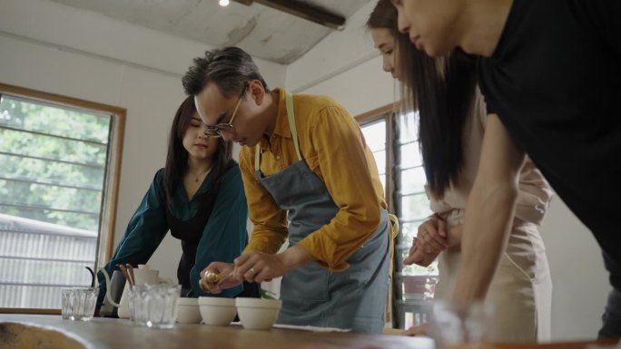 亚裔华裔男咖啡师舀咖啡渣清洗杯饮范围，从桌上的陶瓷杯上撇去咖啡渣-库存视频