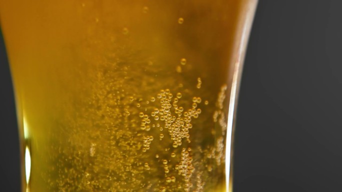 在微距特写中饮用透明玻璃啤酒饮料。酒精饮品文化节或碳酸饮料现代派对。工作室拍摄的抽象酿造或琥珀液体服