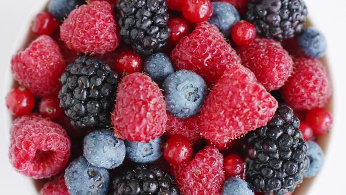 健康的水果浆果。新鲜水果小吃。夏季概念新鲜覆盆子，黑莓，蓝莓，红醋栗旋转在一个孤立的白色背景顶部视图