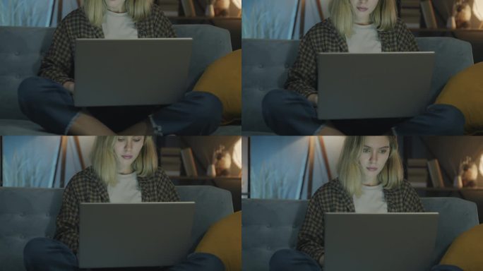 美丽的年轻女性自由职业者的倾斜肖像，晚上在家里的沙发上用笔记本电脑工作
