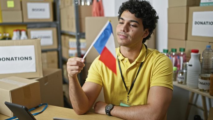 年轻的拉丁男子志愿者手持法国国旗在慈善中心微笑