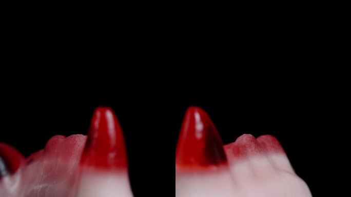 垂直视频。有嚼劲的软糖，形状像红色的吸血鬼尖牙，旋转着。孤立在一个黑色的背景。