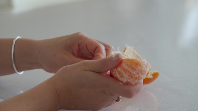 女性的手在餐桌上剥橘子