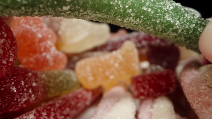 各种颜色、形状和口味的软糖被分散开来，相机从里面穿过它们。多莉滑块极端特写。