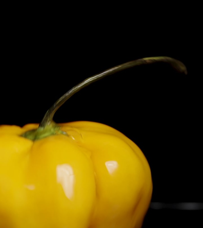 垂直视频。一个黄色的哈瓦那辣椒落入水中，水溅在黑色背景上，慢动作。