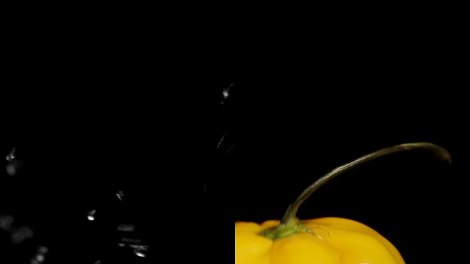 垂直视频。一个黄色的哈瓦那辣椒落入水中，水溅在黑色背景上，慢动作。