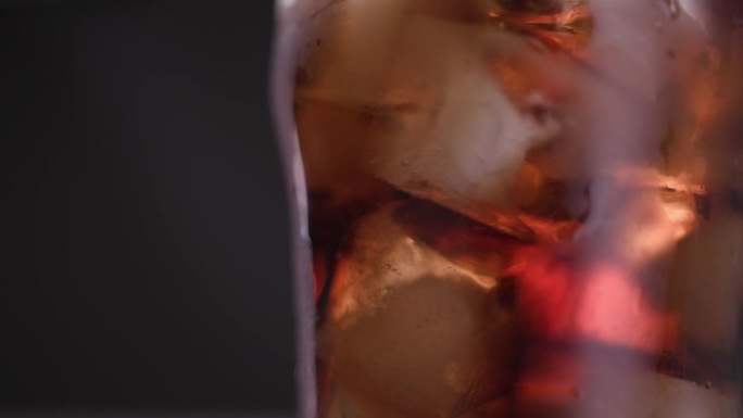 喝可乐的玻璃杯与冰块和湿表面近距离。在微距拍摄下喝汽水或健怡可乐。吃色彩鲜艳的酒吧餐或含高糖液体的快