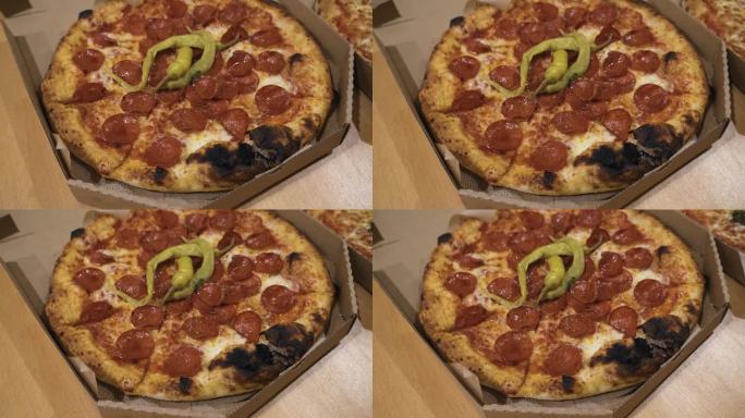 整张意大利辣香肠披萨的俯视图，上面有绿色的辣椒，放在桌子上的纸板披萨盒里