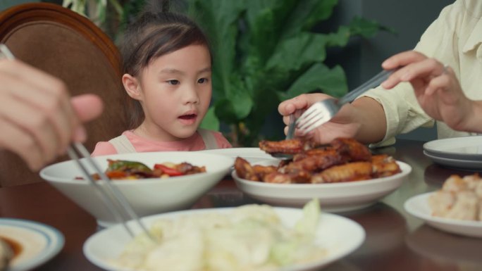 年轻的亚洲家庭坐在后院的餐桌上吃着食物，玩得很开心。多代同堂的家庭一起享受消费。
