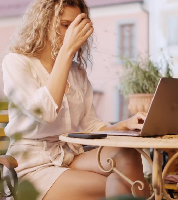 在Ptuj - VERTICAL老城的户外咖啡馆里，金发卷发的女人正在用笔记本电脑工作
