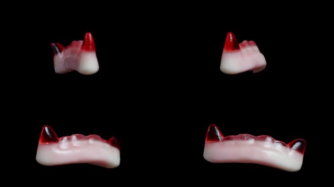 有嚼劲的软糖，形状像红色的吸血鬼尖牙，旋转着。孤立在一个黑色的背景。