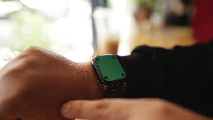 男子在咖啡店休息时触摸和滑动绿色屏幕的智能手表