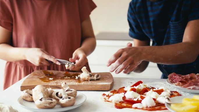 一对夫妇在厨房里一起在披萨上切蘑菇和加蘑菇的特写