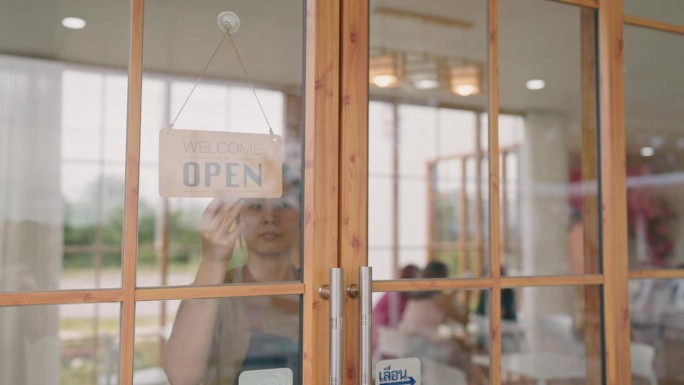 年轻的女老板在咖啡店的窗户上挂着一个开放的牌子