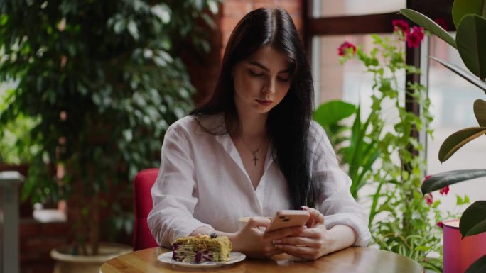 博主女子在咖啡馆休息，在社交媒体上分享内容，女孩使用智能手机的照片