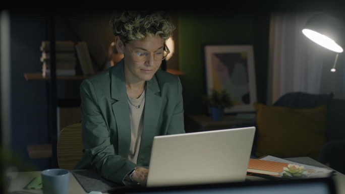 晚上在家里用笔记本电脑工作的年轻女子专注于商业活动