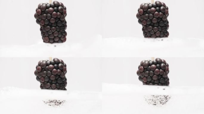 在白色背景上用慢动作将黑莓倒入气泡水中。
