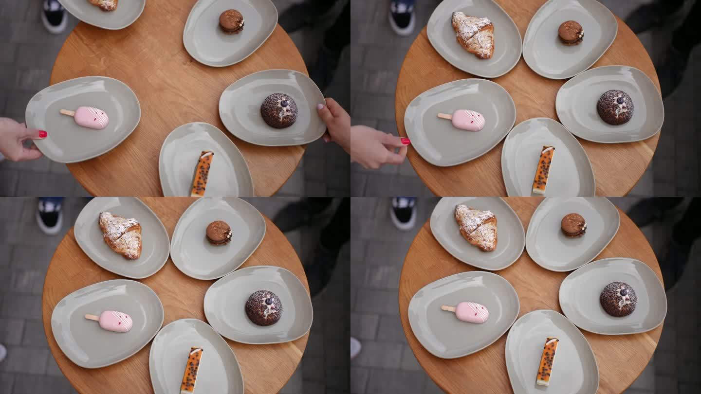 俯视图圆形木桌，年轻的白种人手摆着盘子，上面放着美味的甜点。特写:咖啡厅里，面面相觑的男男女女享用美