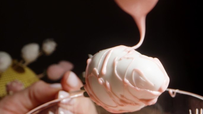 一个女人用白巧克力装饰草莓的特写镜头，她把粉红色的巧克力滴在草莓上。