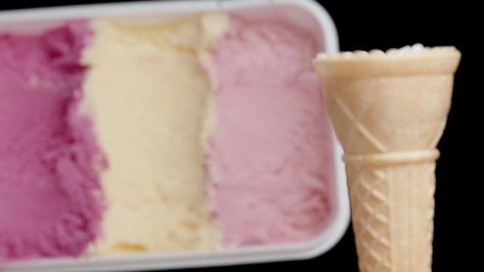 一个空的华夫蛋筒和一盒黑色背景的彩色粉色冰淇淋。