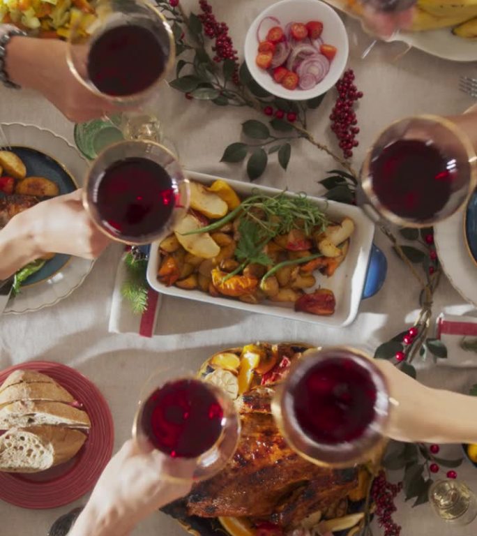 垂直屏幕:父母和客人在一个舒适的家里一起享受圣诞晚餐。亲戚们一起吃饭，举杯喝红酒，举杯祝酒，庆祝节日