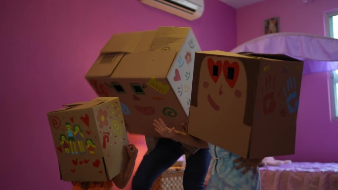 父亲和女儿在家里的卧室里顶着纸板箱玩耍
