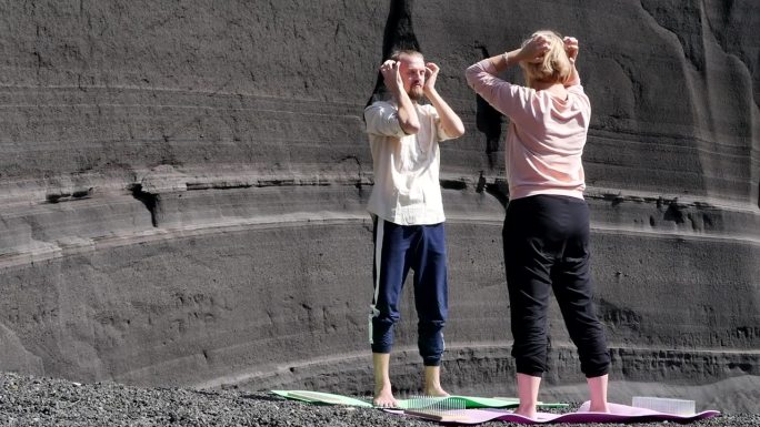 一个年轻的男人和一个女人正在山上的灰色火山渣岩石中冥想，用手指触摸和轻轻地按压他们的头部。瑜伽和苦修