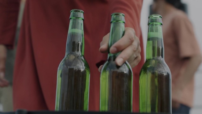 户外聚会上的啤酒瓶特写，女性和朋友们一起牵着手喝酒