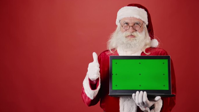 快乐的圣诞老人拿着笔记本电脑与Chromakey屏幕和显示大拇指向上