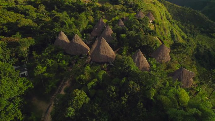 一套南美土著茅草小屋在日落时被丛林包围。空中