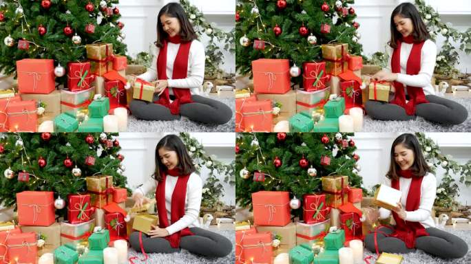 亚洲妇女在圣诞树下打开圣诞礼盒，收到了惊喜礼物。亚洲妇女在客厅里打开礼盒，坐在装饰精美的球圣诞树下庆