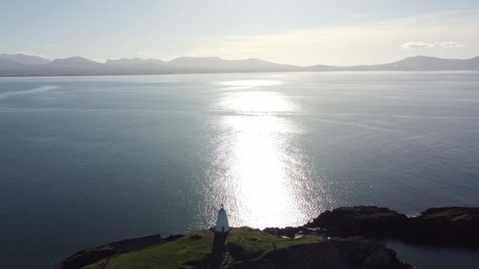 鸟瞰图横跨yynys Llanddwyn灯塔移动通过闪烁的爱尔兰海在日出与朦胧的斯诺多尼亚山脉