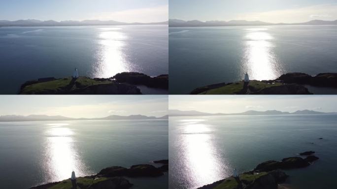 鸟瞰图横跨yynys Llanddwyn灯塔移动通过闪烁的爱尔兰海在日出与朦胧的斯诺多尼亚山脉