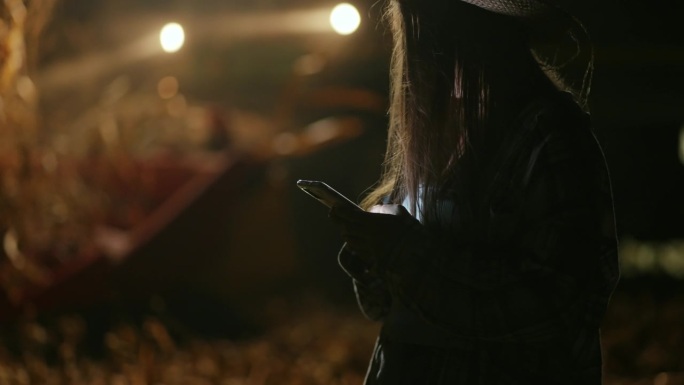 Sunhat的农民在夜间观看联合收割机收割时使用手机