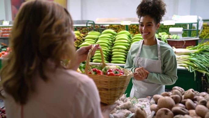 友好的非裔美国小贩将一篮子新鲜蔬菜和水果递给在市场取货的顾客