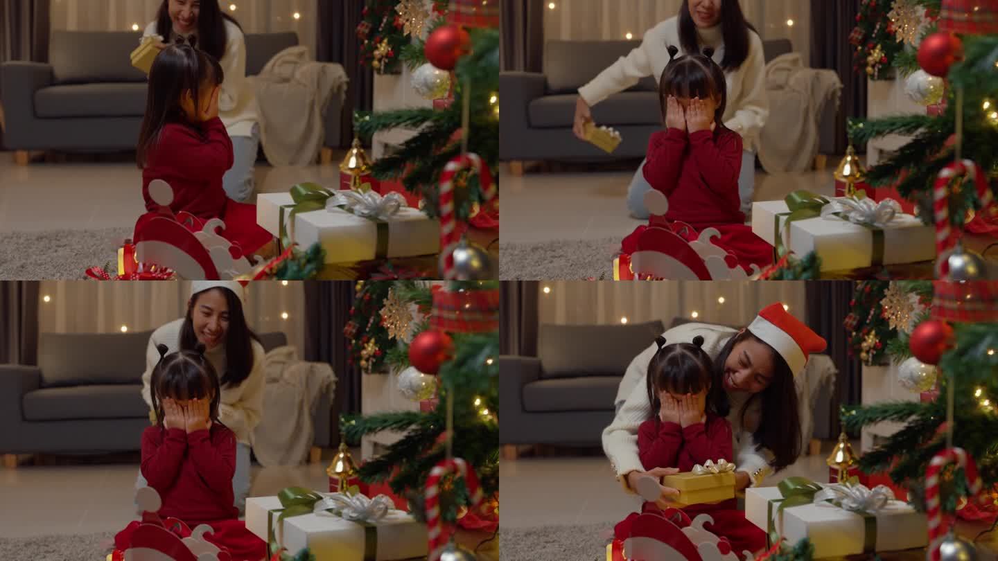亚洲幸福的家庭享受庆祝新年假期聚会一起在家里晚上。小女孩们坐在地毯地板上，闭着眼睛等着圣诞树旁妈妈送