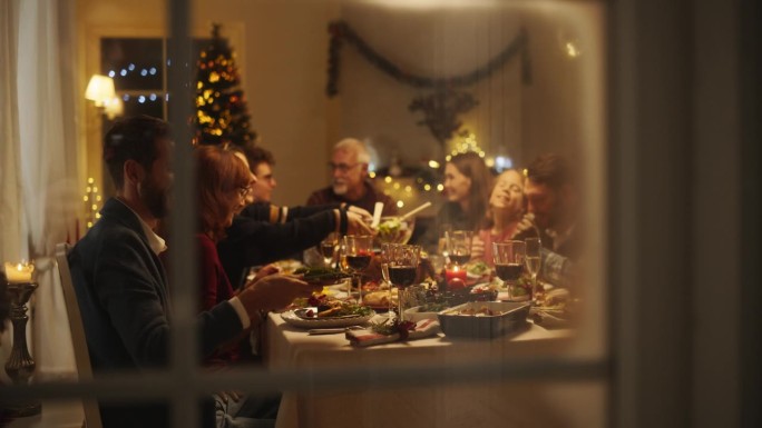 快乐的家庭团聚在家里吃传统的圣诞晚餐，烤火鸡。客厅里挤满了享用节日菜肴的老人和年轻人。透过雪窗的创意